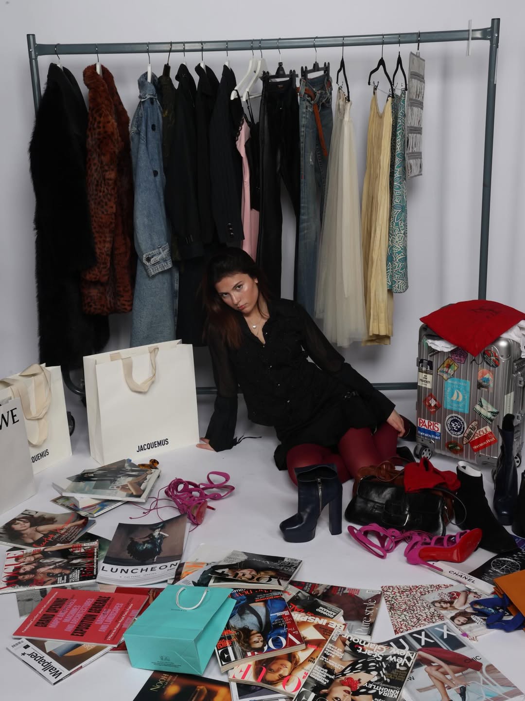 Charlee seated among a styled rail of clothes, magazines, and accessories